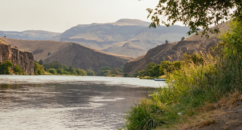 A calm Deschutes river flows between a mountainous desert landscape. 